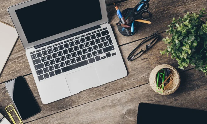 A laptop on a wooden desk with a plant and other items.
